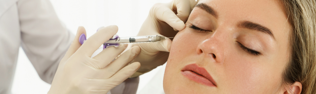 Gloved practitioner administering a facial filler injection to a woman’s cheek.